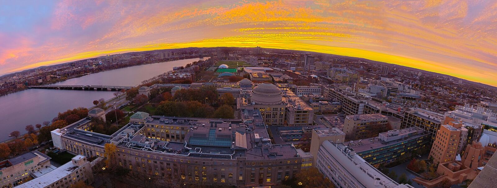 Aerial view of the MIT campus, with the Charles River on the left. The clouds are yellow, and there is a purple tint to the photo.